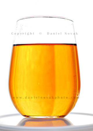 Take notes on lighting setup. Glass of golden tea with vertical bands of light and shadow adding depth on white background.
